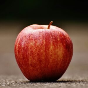 A vibrant red apple resting on a textured outdoor surface, showcasing natural beauty and freshness.