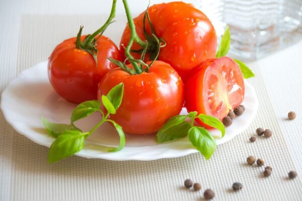 A fresh and vibrant display of tomatoes, basil, and peppercorns on a white plate, perfect for healthy cooking.